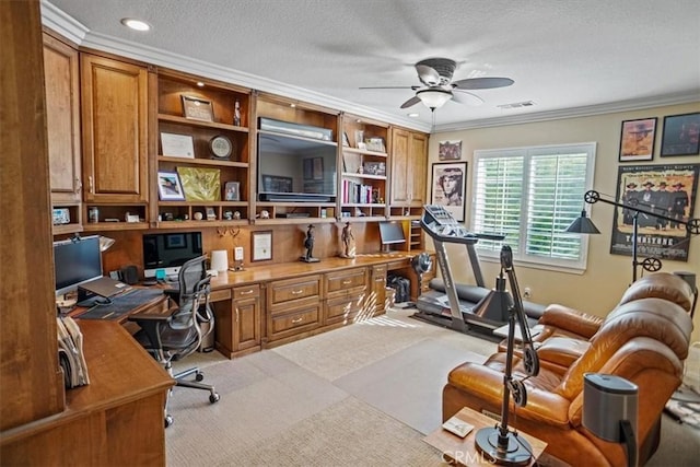 carpeted home office featuring built in desk, a textured ceiling, ornamental molding, and ceiling fan