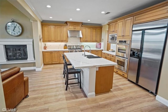 kitchen featuring a kitchen island with sink, built in appliances, light stone countertops, a breakfast bar, and sink