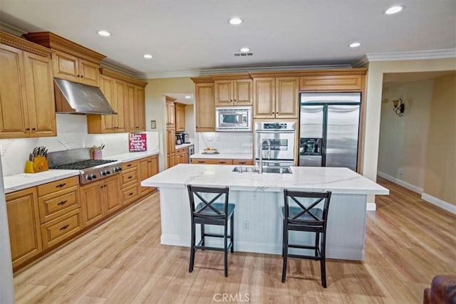 kitchen with built in appliances, an island with sink, light wood-type flooring, crown molding, and a breakfast bar area