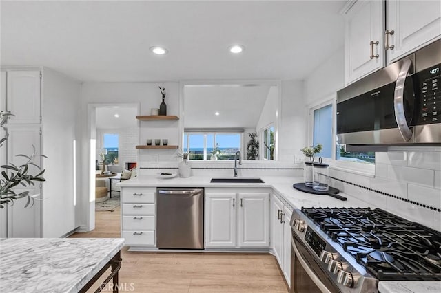 kitchen with tasteful backsplash, sink, light wood-type flooring, stainless steel appliances, and white cabinets