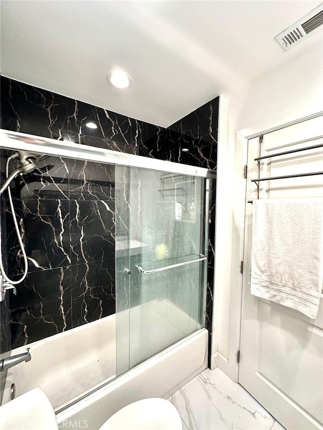 bathroom featuring toilet and bath / shower combo with glass door