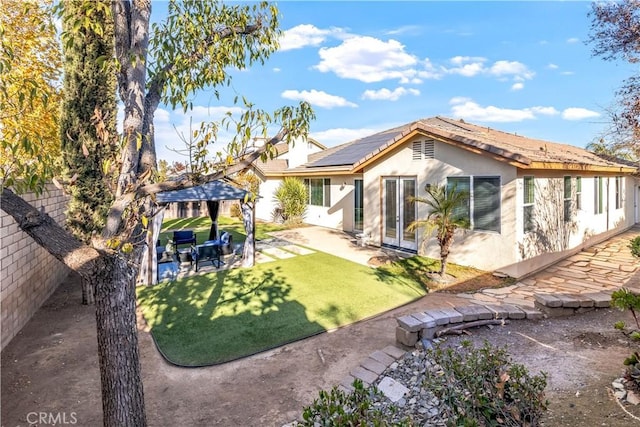 back of house with stucco siding, a fenced backyard, a gazebo, solar panels, and a patio area