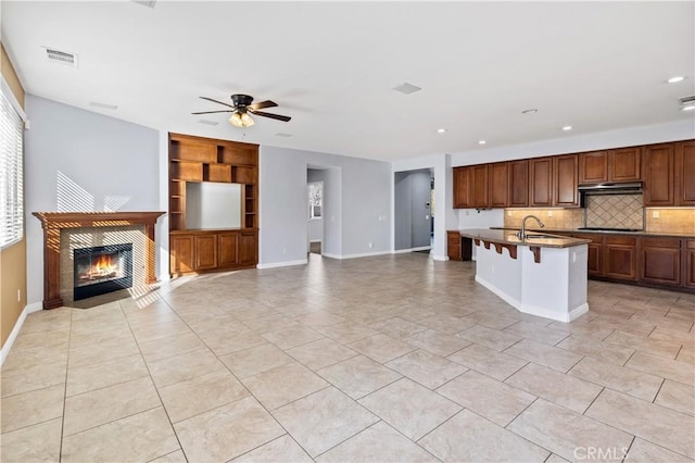 kitchen featuring visible vents, a fireplace, a sink, under cabinet range hood, and black stovetop