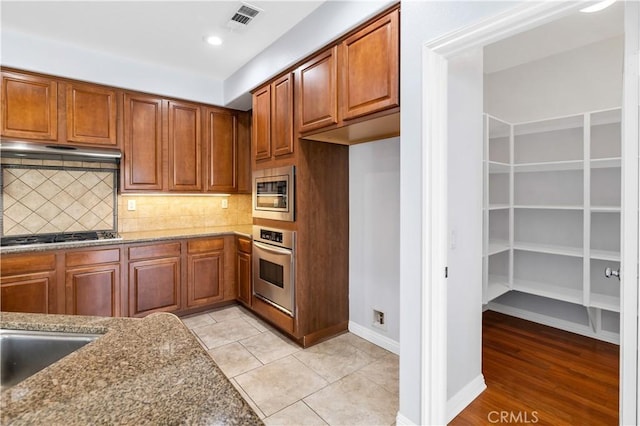 kitchen featuring visible vents, under cabinet range hood, light stone counters, tasteful backsplash, and stainless steel appliances