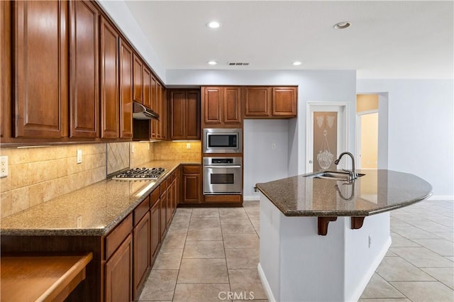 kitchen featuring dark stone counters, light tile patterned flooring, a sink, stainless steel appliances, and under cabinet range hood