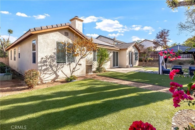 rear view of property featuring stucco siding, a lawn, fence private yard, and a chimney