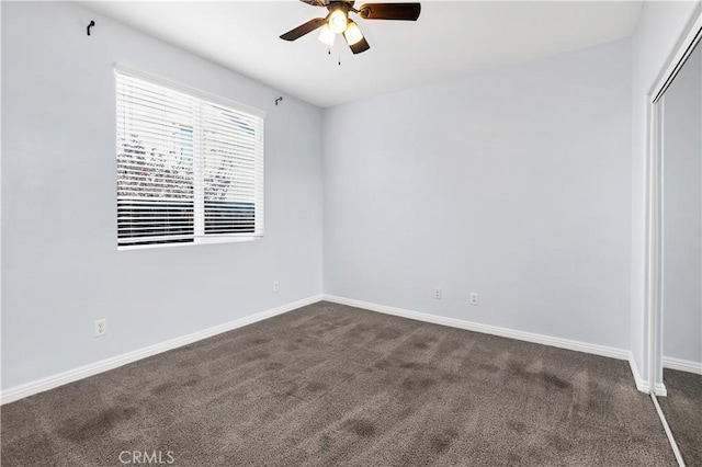 unfurnished room with dark colored carpet, baseboards, and a ceiling fan