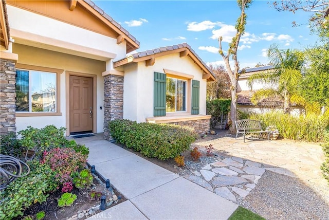 doorway to property with stone siding, stucco siding, and a patio