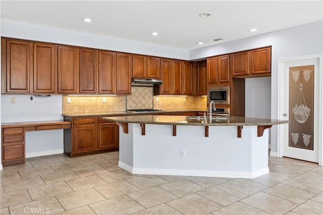 kitchen featuring under cabinet range hood, appliances with stainless steel finishes, brown cabinetry, and a sink