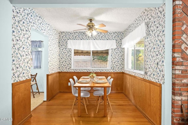 dining area with ceiling fan, wood walls, light wood-type flooring, a textured ceiling, and breakfast area