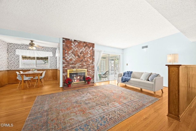 living room featuring a textured ceiling, ceiling fan, a fireplace, and hardwood / wood-style floors