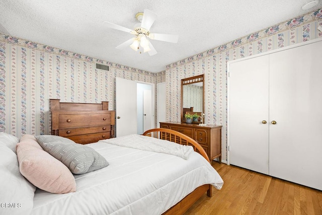 bedroom with a textured ceiling, ceiling fan, a closet, and light hardwood / wood-style flooring