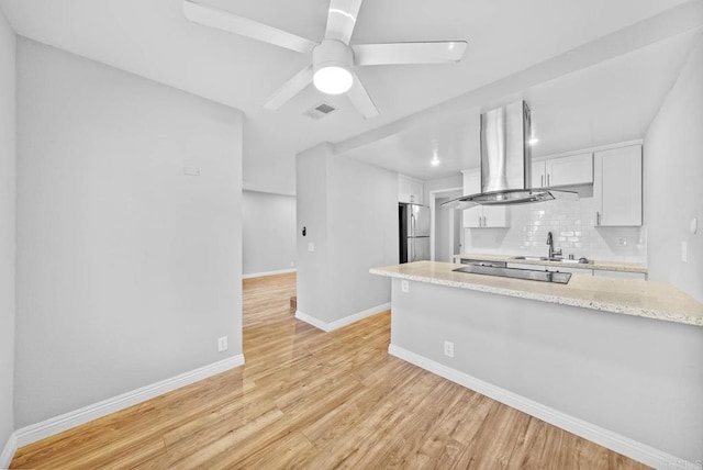 kitchen with decorative backsplash, stainless steel refrigerator, white cabinets, island range hood, and light stone counters