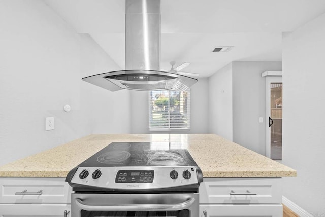 kitchen with island exhaust hood, light stone counters, white cabinetry, and stainless steel electric range oven