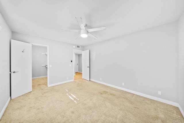 unfurnished bedroom with a spacious closet, a closet, light carpet, and ceiling fan