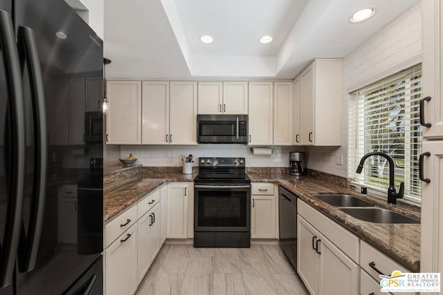 kitchen with pendant lighting, black appliances, dark stone countertops, sink, and a tray ceiling