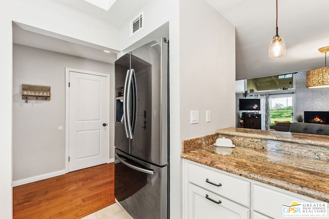 kitchen featuring white cabinetry, light hardwood / wood-style floors, hanging light fixtures, stainless steel fridge, and stone counters