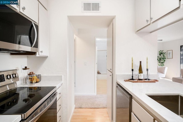 kitchen featuring stainless steel appliances, light hardwood / wood-style flooring, and white cabinets