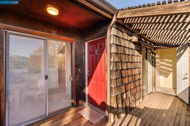 view of exterior entry featuring a deck and a pergola