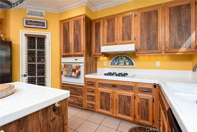 kitchen with sink, white appliances, ornamental molding, tile counters, and light tile patterned floors