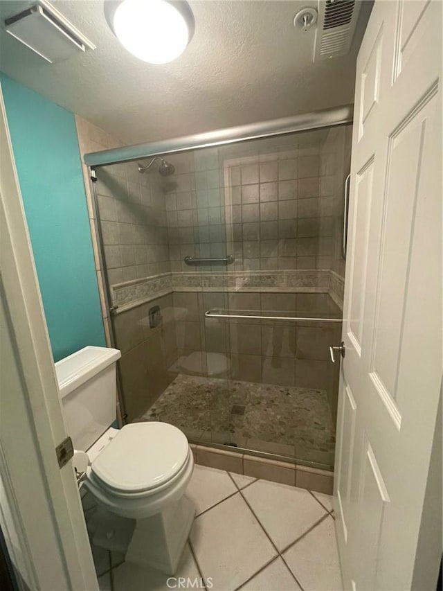 bathroom with a shower with shower door, a textured ceiling, toilet, and tile patterned flooring