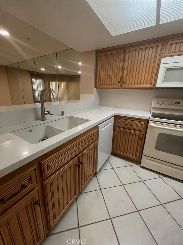 kitchen featuring light tile patterned floors, sink, light stone counters, and white appliances