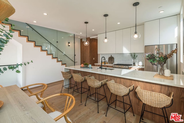 kitchen with decorative backsplash, sink, white cabinetry, light wood-type flooring, and stainless steel fridge