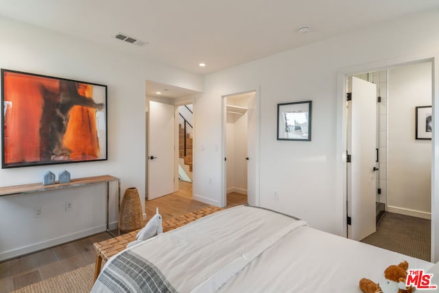 bedroom with a walk in closet and hardwood / wood-style floors