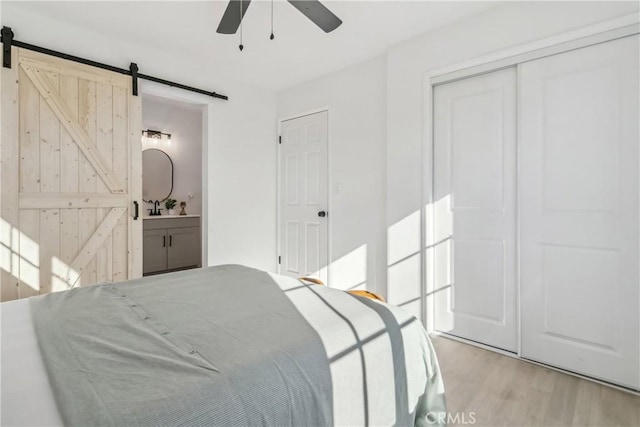 bedroom featuring ensuite bathroom, a barn door, ceiling fan, light hardwood / wood-style flooring, and a closet