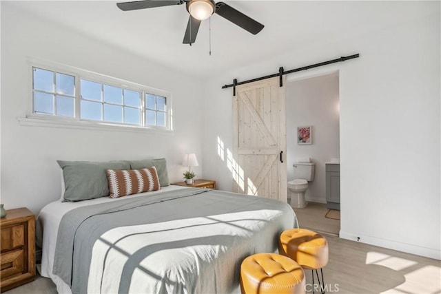 bedroom with ceiling fan, light hardwood / wood-style floors, connected bathroom, and a barn door