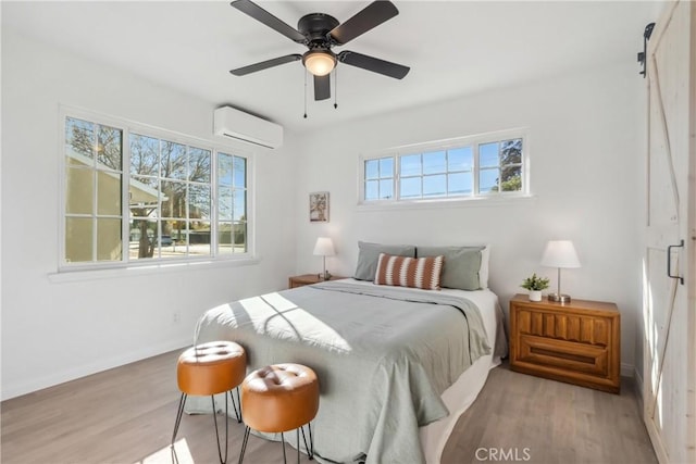 bedroom with ceiling fan, an AC wall unit, and light hardwood / wood-style flooring