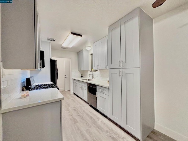 kitchen featuring sink, tasteful backsplash, light hardwood / wood-style flooring, stainless steel dishwasher, and stove