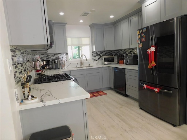 kitchen featuring visible vents, backsplash, gray cabinets, freestanding refrigerator, and a sink