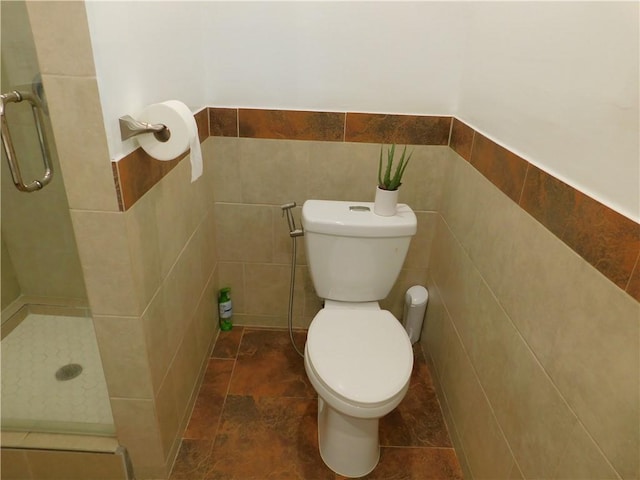 bathroom with wainscoting, toilet, a stall shower, and tile walls