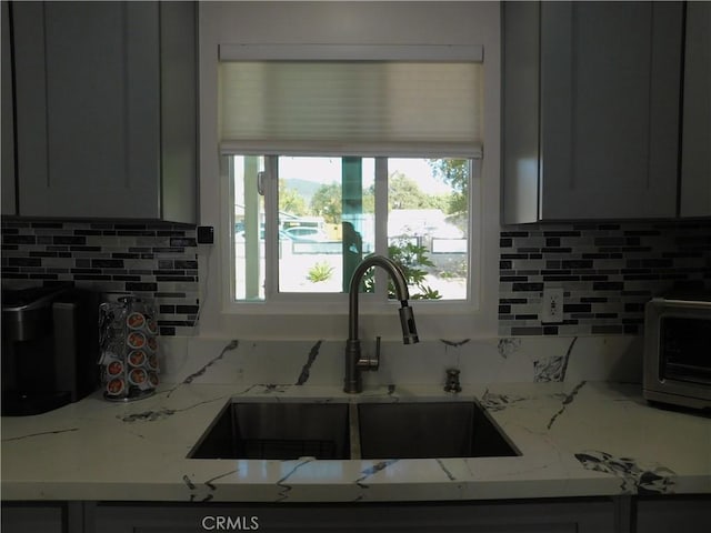 kitchen with a toaster, light stone counters, backsplash, and a sink