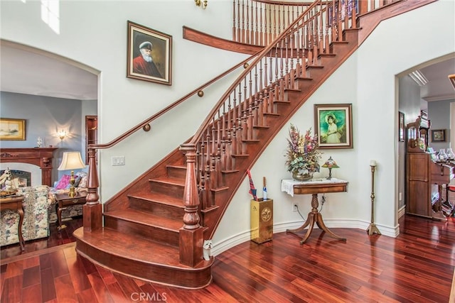 stairs featuring arched walkways, a fireplace, baseboards, wood-type flooring, and a high ceiling