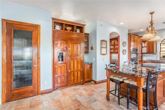 kitchen featuring baseboards, dark stone countertops, brown cabinets, and stone tile flooring
