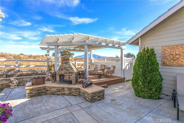 view of patio featuring an outdoor stone fireplace, a mountain view, a pergola, and fence