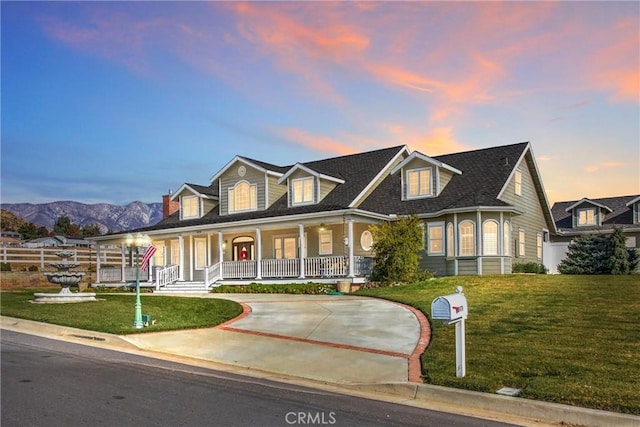 cape cod home with covered porch, a mountain view, and a lawn