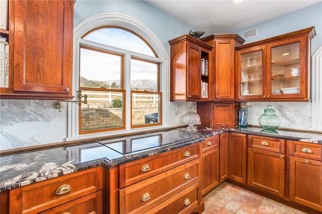 kitchen featuring dark stone counters, stone finish flooring, and backsplash