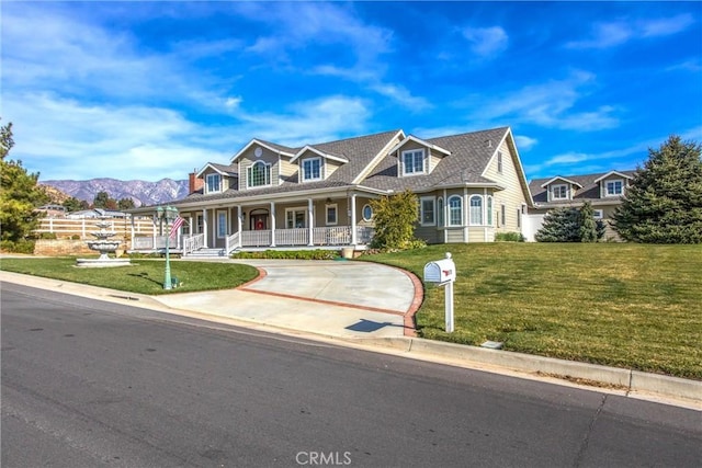 view of front of property featuring covered porch, concrete driveway, a mountain view, and a front yard