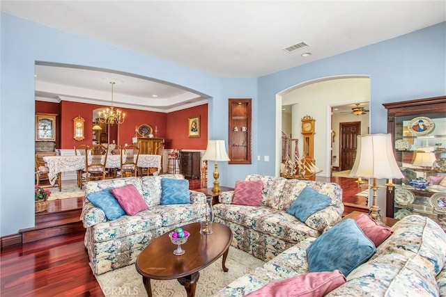 living area featuring visible vents, crown molding, arched walkways, wood finished floors, and a chandelier