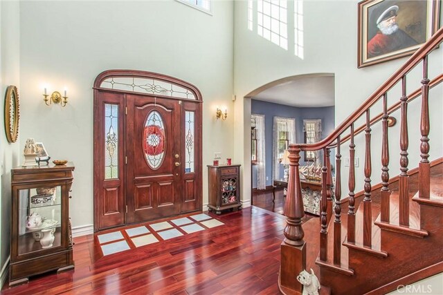 entryway with a towering ceiling, arched walkways, wood finished floors, stairway, and baseboards