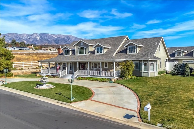 view of front of property with a front lawn, fence, curved driveway, a porch, and a mountain view