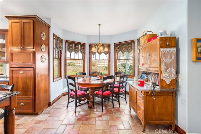 dining space with baseboards, a chandelier, and stone tile flooring