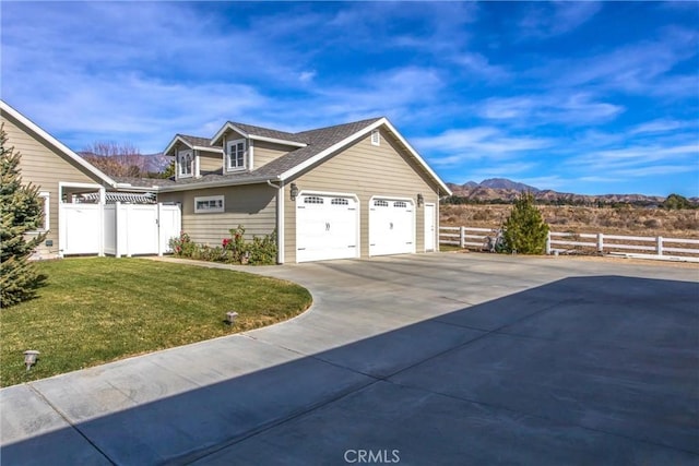 view of side of home with fence, driveway, an attached garage, a mountain view, and a yard