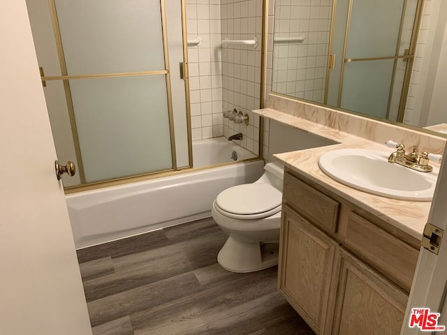 full bathroom with toilet, vanity, wood-type flooring, and shower / bath combination with glass door