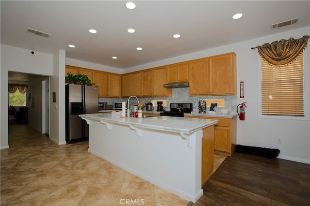 kitchen featuring electric range oven, a kitchen bar, sink, stainless steel fridge, and a center island with sink