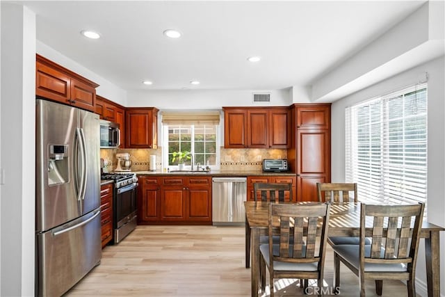 kitchen with tasteful backsplash, appliances with stainless steel finishes, sink, and light hardwood / wood-style flooring