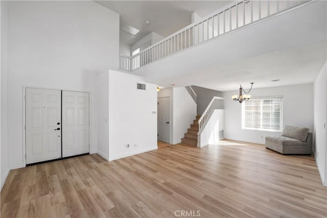 entryway with light wood-type flooring, a towering ceiling, and a chandelier